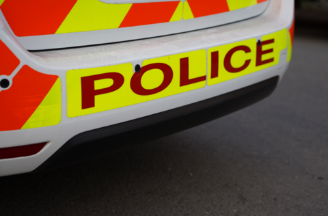 The rear of a police car, with red letters spelling out POLICE and red and yellow stripes over the boot and bumper area