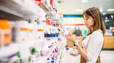 Woman looks at shelf of medicines at pharmacy 