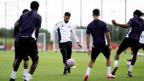 Ruben Amorim kicking a football during Manchester United training. There are four players with their backs to the camerea.