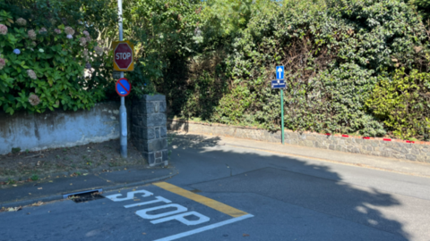 A picture of Green Lanes in Guernsey. The road has white paint on it which states 'STOP' with a yellow line above it at the junction.