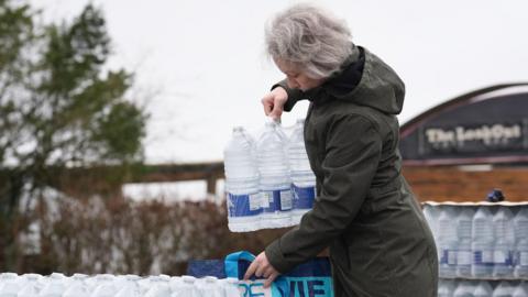 A woman lifts bottled water from a stack of bottled water
