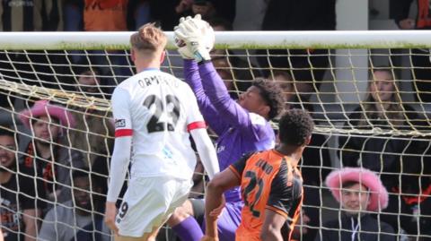 Danny Ormerod in a white AFC Fylde kit challenges a goalkeeper for the ball