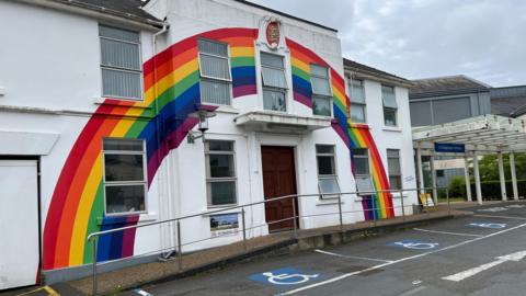 The front of a hospital building with a rainbow painted on it. Disabled parking spaces in front.