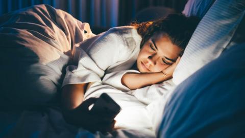 Someone looking at their phone in bed with the light off.