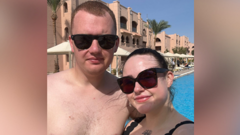 A man and woman wearing sunglasses. They're standing in a pool area.