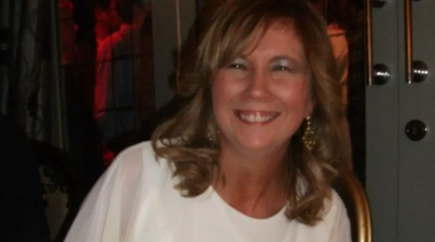 A woman with long hair who is wearing a white top is smiling at the camera