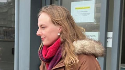 Dr Beth Upton - a transgender woman with long blonde hair, a red scarf and a brown jacket - leaves a building