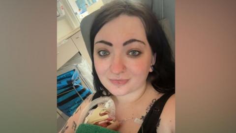Rebecca Price is sitting on a hospital chair and holding her baby boy Levi on her chest. Levi is attached to medical equipment including a breathing tube. 
