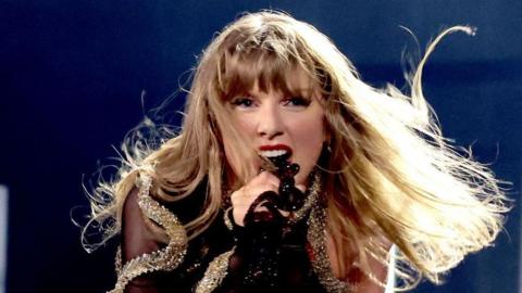 Taylor Swift performs on stage in December last year in Vancouver, Canada, as part of her Eras tour. She is singing passionately into the microphone and is wearing a black and gold sequinned outfit.