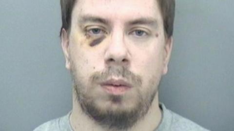 Police custody photograph of Stephen Cole. He has brown hair, a beard and a black eye.