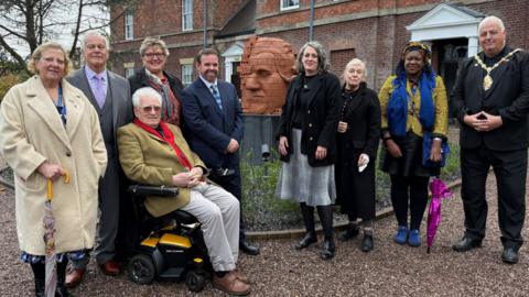 A group of people standing next to a brick-built sculpture showing the partial face of Josiah Wedgwood with a building visible behind.