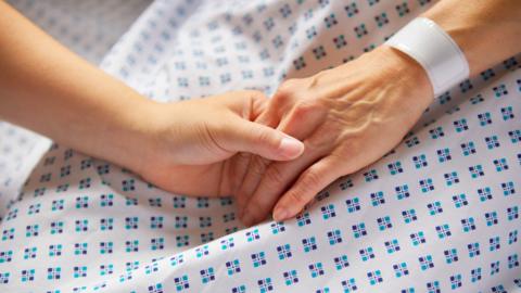 Two people hold hands on a hospital bed 