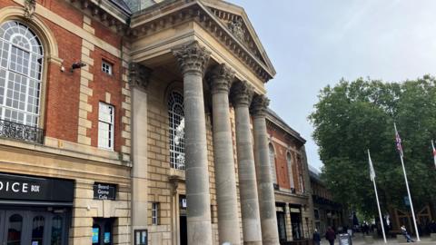 Outside of Peterborough town hall, where there are four large columns in front of the brick building in the city centre.