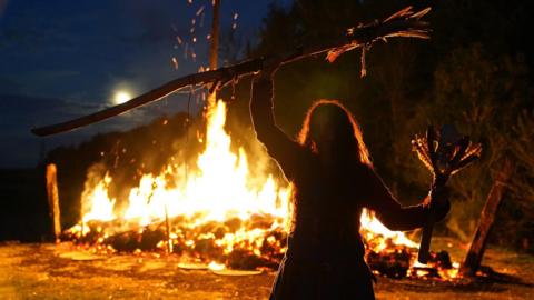 Re-enacted scene of a Viking woman holding a stick above her head in front of a firey scene