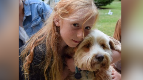 A picture of Ruth Szymankiewicz, who has long ginger hair, cuddling a terrier dog.