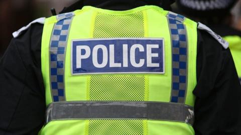 The back of a police officer wearing a yellow high-vis jacket that has POLICE written on it.