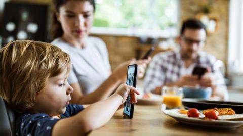 Family using phones at the dinner table.