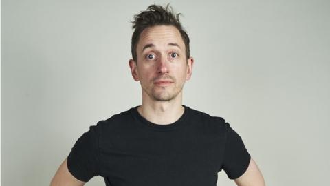 John Robins in a short-sleeved black t-shirt.