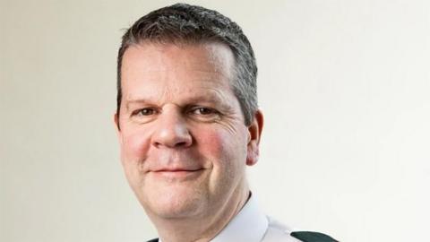 Close up portrait picture of Chris Todd with short dark hair wearing a white police shirt with green epaulettes 