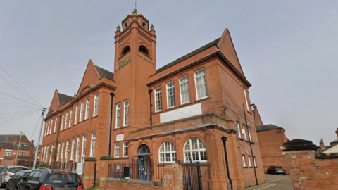 A large redbrick Victorian former school building with a bell tower