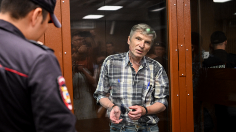 Moscow city deputy Alexei Gorinov stands inside a glass cell during the verdict hearing in his trial at a courthouse in Moscow in July 2022