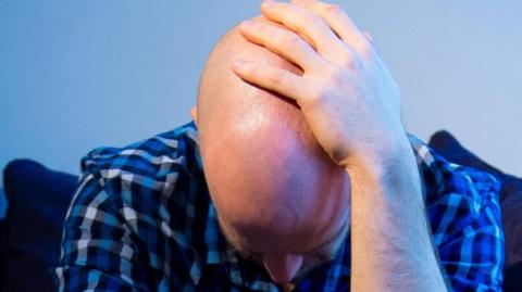 Man wearing a blue checked shirt with his hand on his head