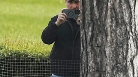 A picture of a Southampton employee holding a photo next to a tree at Middlesbrough's training ground