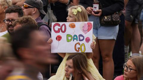  A young girl holds a homemade placard saying "Go Dad go" as runners pass by.
