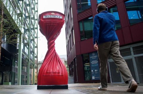 A man walks towards a twisted red phone box, an art creation by Alex Chinneck in Bristol