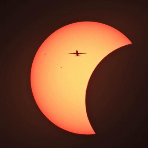The sun is behind the moon during the eclipse, with the silhouette of a plane in front.