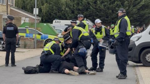 A group of police around a man being arrested on the ground.
