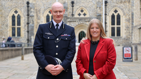 Alexis Boon, standing in police uniform and holding a police hat, stood next to Donna Jones, who is wearing a red jacket and a black top underneath it.