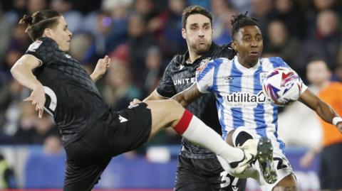 Huddersfield Town's Tawanda Chirewa (27) is tackled by Wrexham's George Dobson (15)