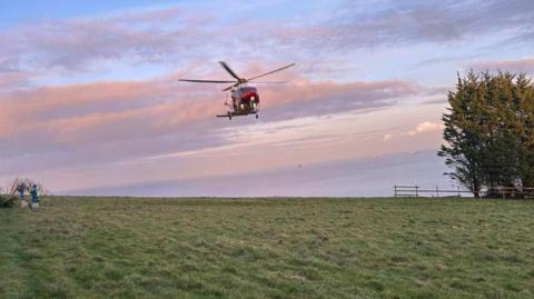 A helicopter landing on a green field.