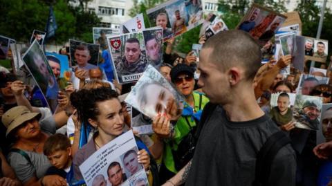 A Ukrainian prisoner of returns to a crowd of people holding posters bearing the faces of missing soldiers