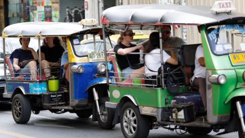 Tourists travel on tuk-tuk taxis in Bangkok.