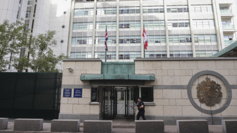 A guard in a black outfit walks past the gated entrance to the British Embassy, a several-storey high office block, in Moscow