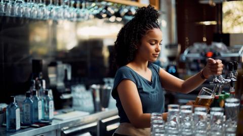 Young waitress pouring draft beer while working at bar counter. 