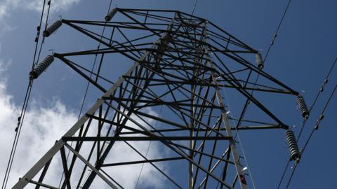 Looking up from the ground to a giant dual-line electricity pylon against a blue sky