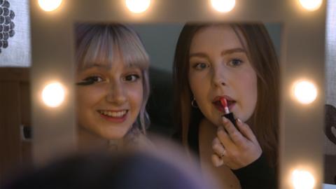 Two young women applying make up in a mirror