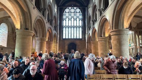 Large group of people, some sitting, some standing, inside Southwell Minster, waiting to see the display