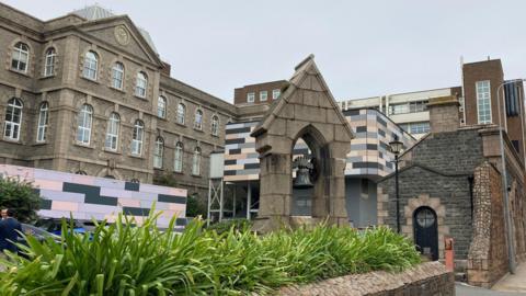 There is a  mix of older stone clad buildings with a small bell-tower in the front. Several buildings have pink, grey and black cladding.