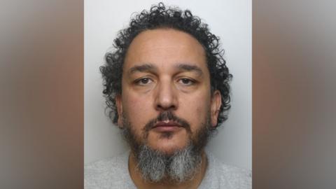 A prison mug shot of a man in a grey t-shirt looking at the camera. 