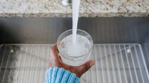 Close-up of woman pouring a glass of water at kitchen sink