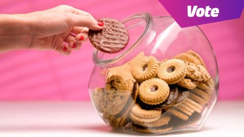 A clear biscuit tin with biscuits in it. A hand is reaching in and picking up