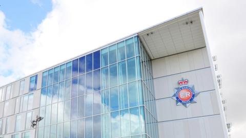 A white building with glass windows and a Greater Manchester Police sign/badge on the right hand side of the building 