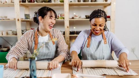 Two women attend a pottery classic, both are smiling.