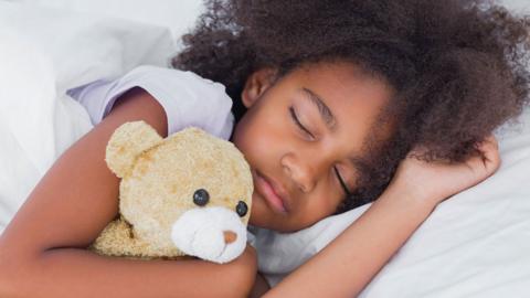 A toddler asleep cuddling a teddy bear