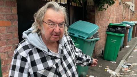 Michael Eaton, who lives on Lawson Street, stood in the road pointing at overflowing rubbish on the road.