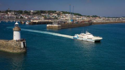 A passenger ferry leaving St Peter Port Harbour. You can see St Peter Port sea front in the background.